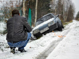 Man looking at car in ditch skidded off road in snow