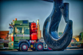 The metal hook of a tow truck with a large truck in the background