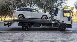 White saloon car on the back of a flat bed tow truck