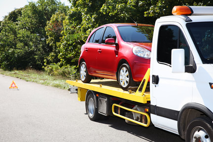 Small red car loaded onto the back of a towing service truck