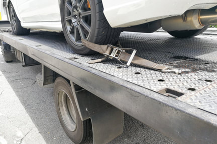 White car secured by tire straps on the back of a flat be tow truck